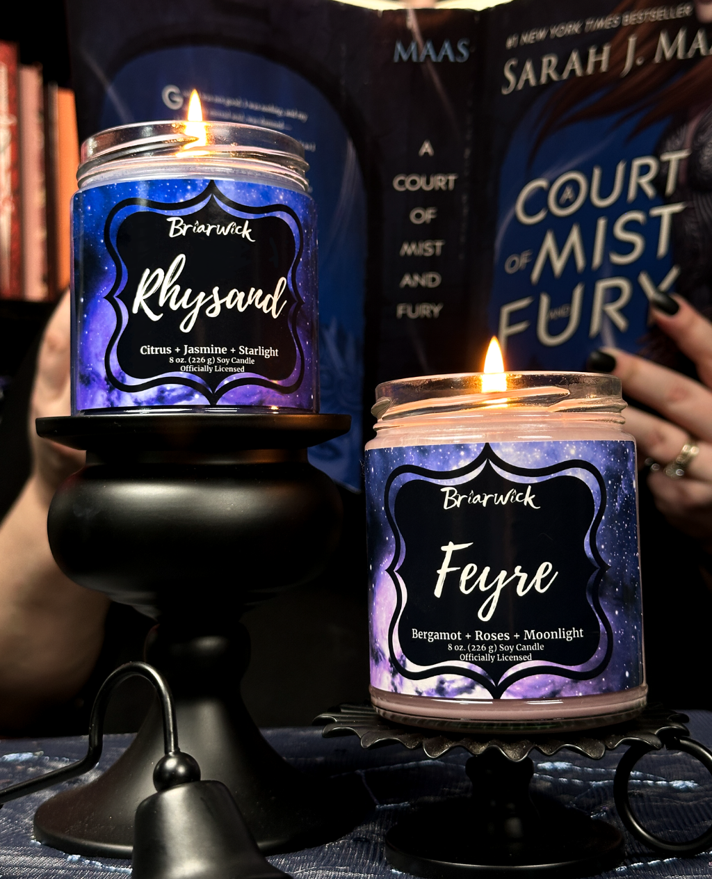 Two lit candles with labels 'Rhysand' and 'Feyre' in front of an open book titled 'Court of Mist and Fury'.