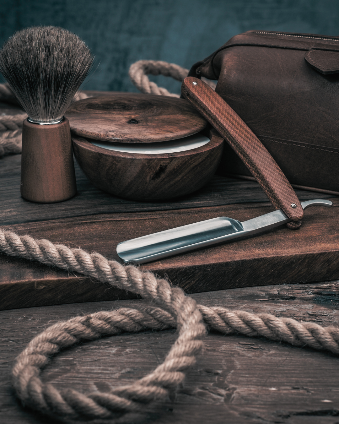 Shaving set with a straight razor, brush, and bag on a wooden surface.