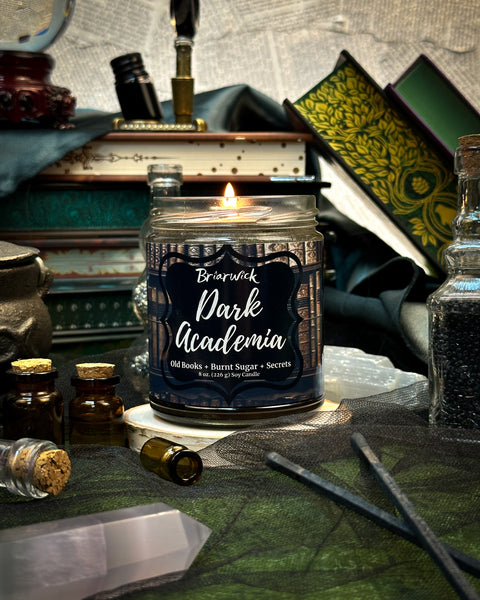 Candle labeled 'Dark Academia' in a scholarly setting with books and quill.