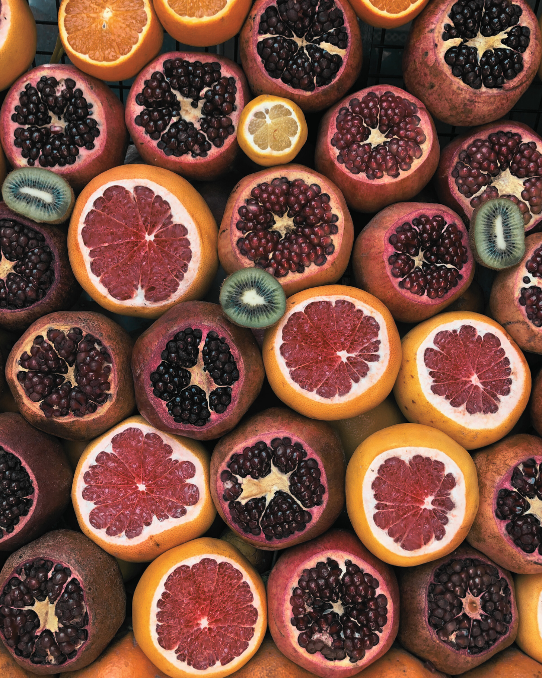 Assorted sliced fruits including blood oranges, pomegranates, and kiwis on a wooden surface.