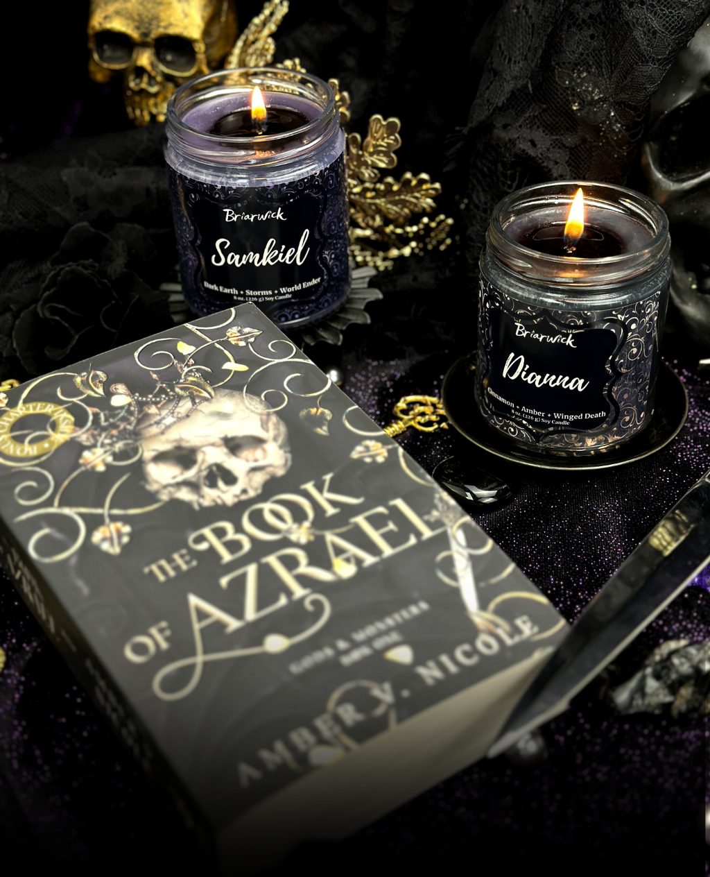 Two lit candles with decorative packaging and a skull-themed book cover titled 'The Book of Azrael' on a dark background.