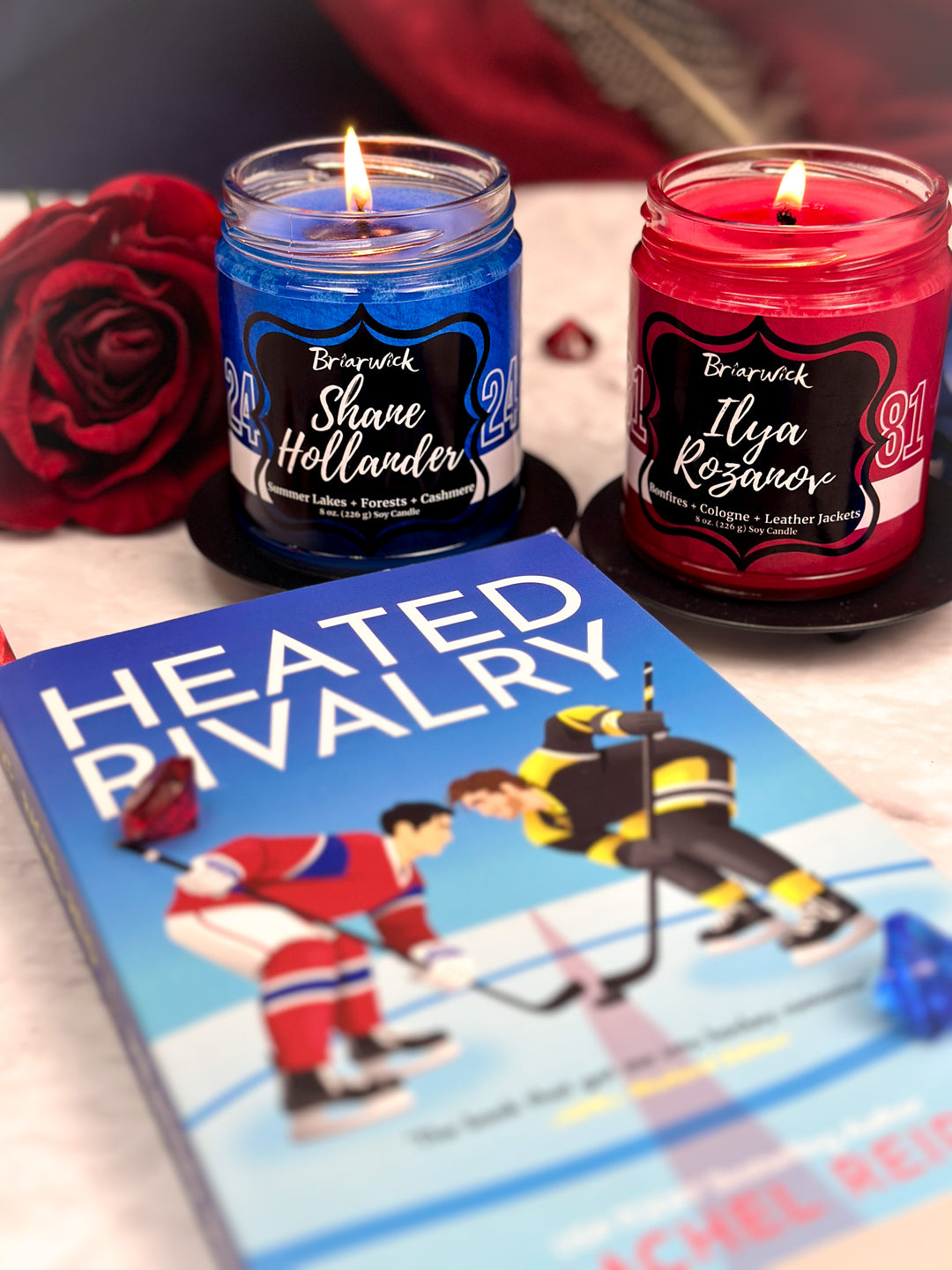 Two candles labeled 'Shave Hollander' and 'Ilya Rozanov' next to a book titled 'Heated Rivalry' on a white surface.