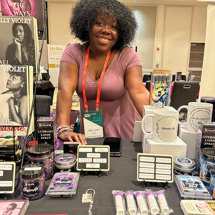 Woman standing behind a table with various products at an event, with books and a magazine in the background.