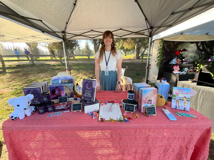 Person standing behind a table with various items under a tent outdoors.