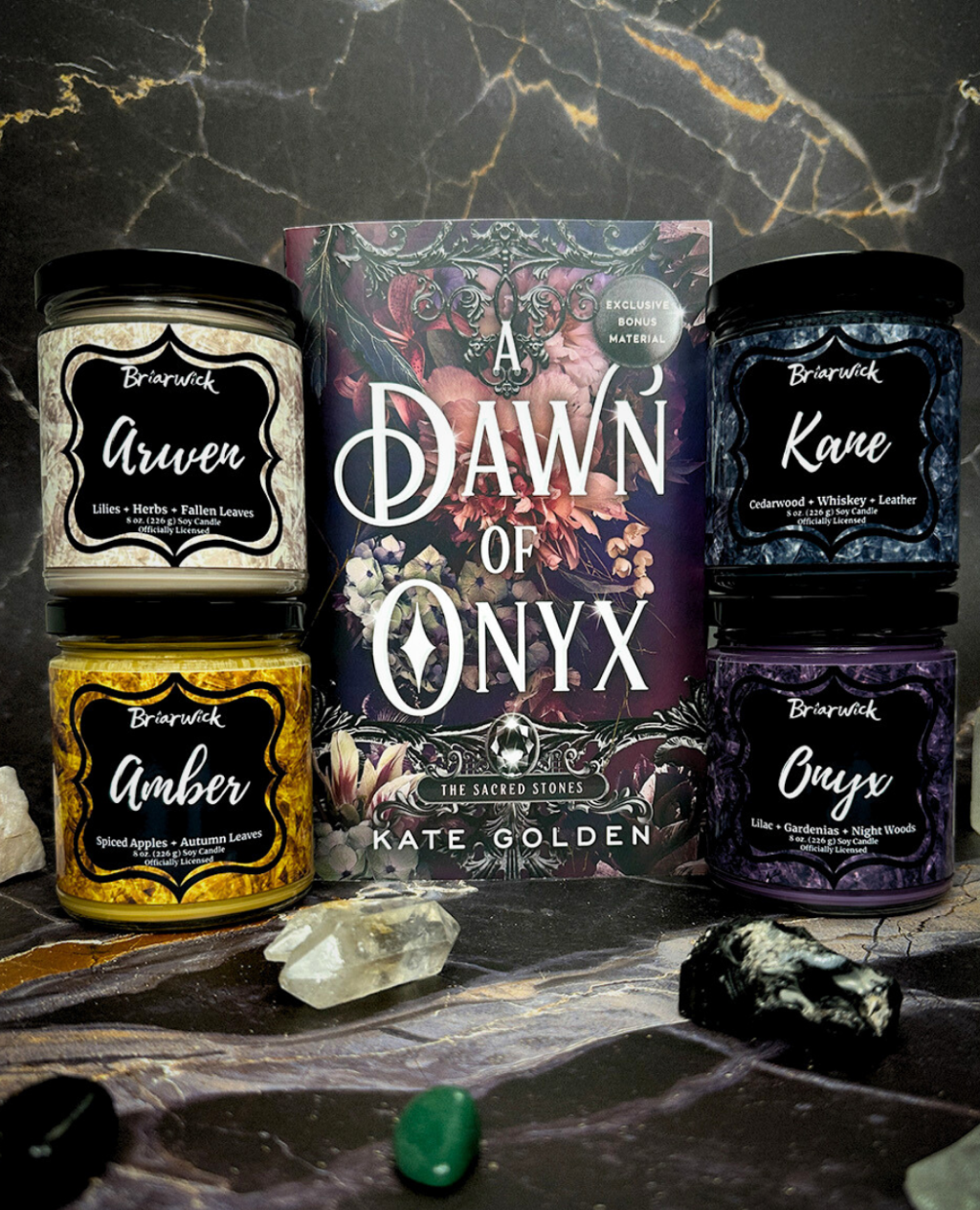 Book titled 'A Dawn of Onyx' by Kate Golden with four stacked candles on a dark marble surface.