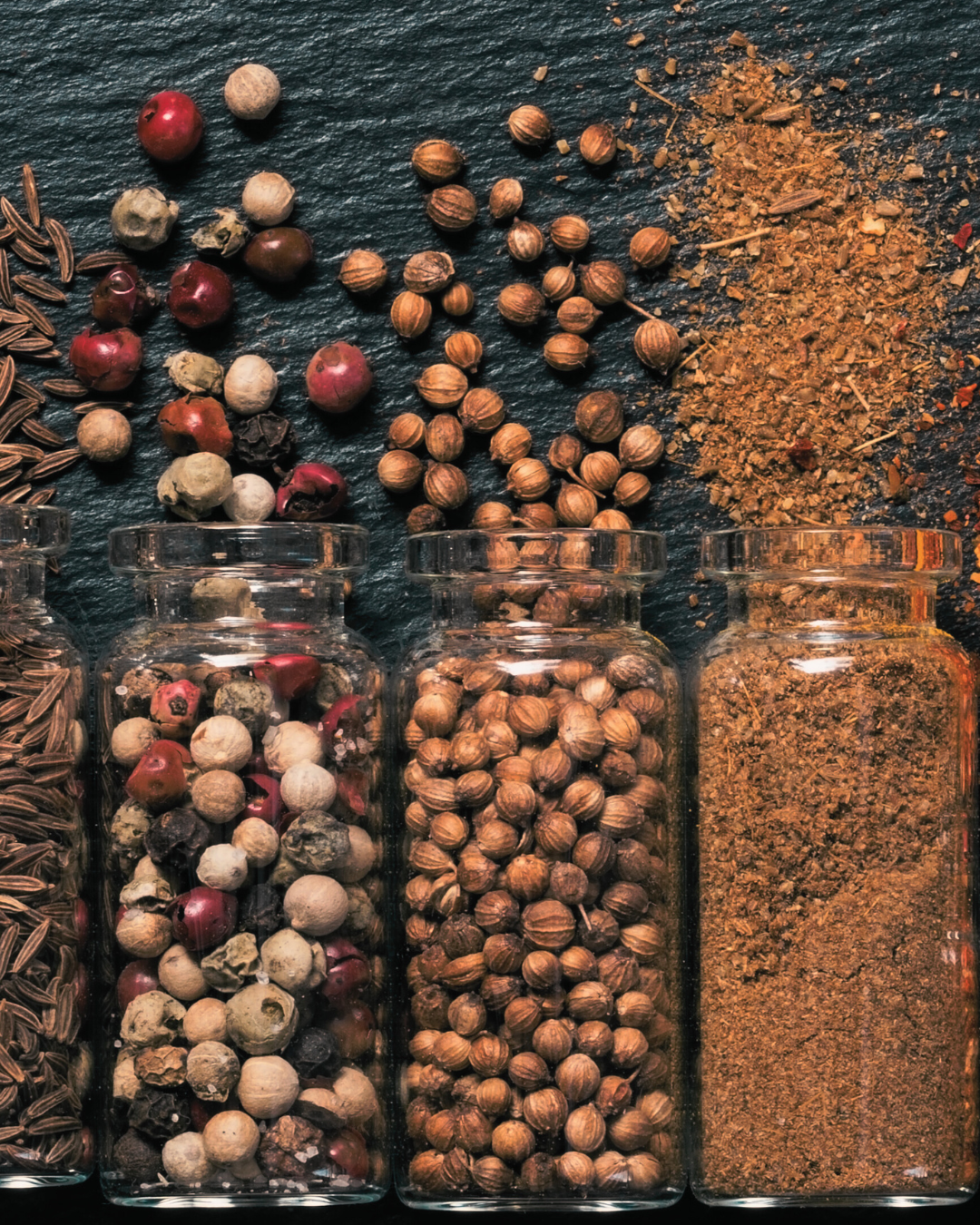 Spices and herbs in glass jars on a dark surface