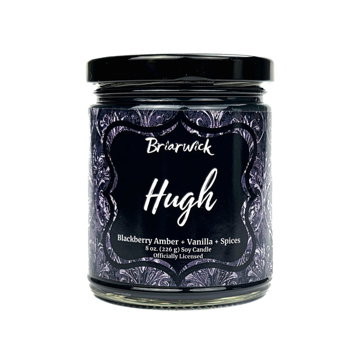 A jar candle labeled Briarwick Hugh, featuring a black lid and a dark label with purple ornate patterns, on a plain white background.