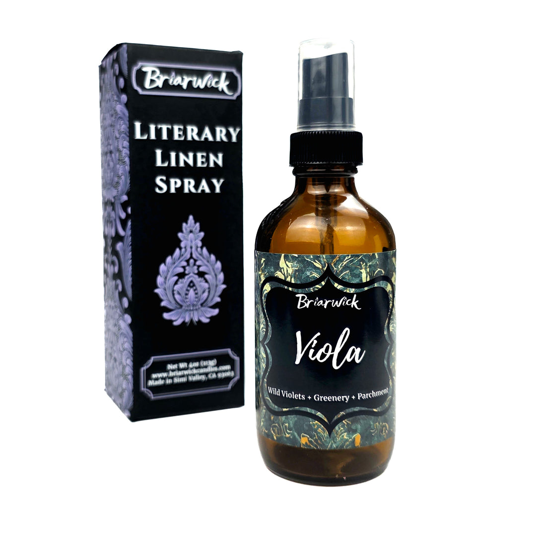 Briarwick Literary Linen Spray bottle with an amber glass body and black spray cap, shown next to its black packaging box with purple ornamental details on a white background.