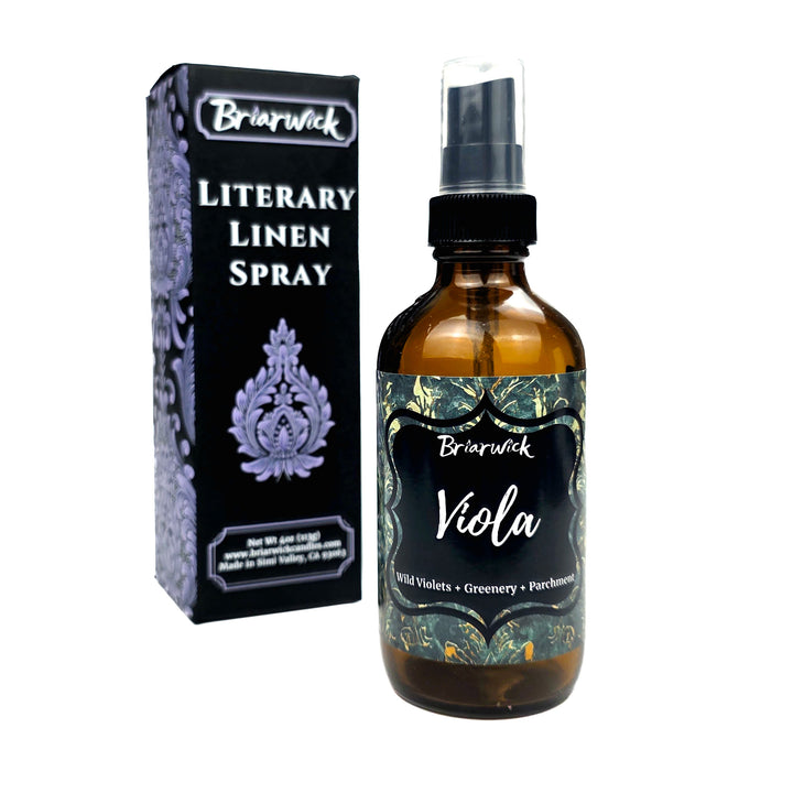 Briarwick Literary Linen Spray bottle with an amber glass body and black spray cap, shown next to its black packaging box with purple ornamental details on a white background.