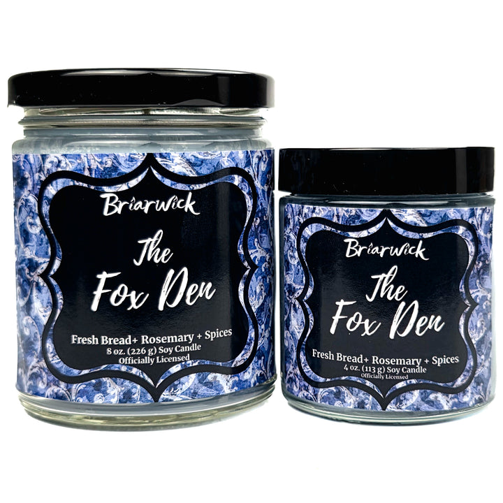 Two glass soy candles with black lids and matching blue-and-white patterned labels reading Briarwick The Fox Den, shown on a white background.