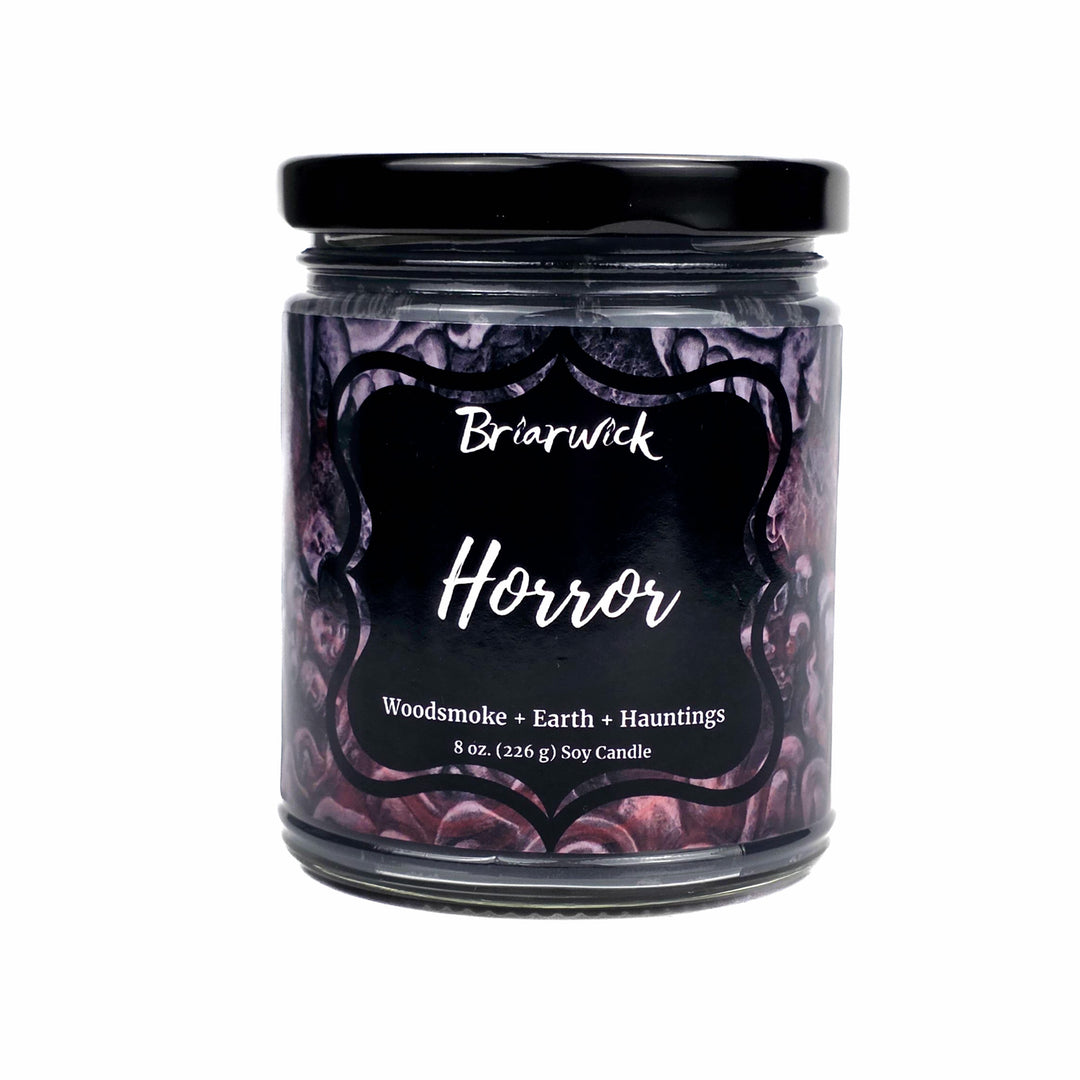 An 8 oz soy candle in a clear glass jar with a black lid and a black label featuring the brand name 'Briarwick' and the scent 'Horror' in white script, set against a plain white background.