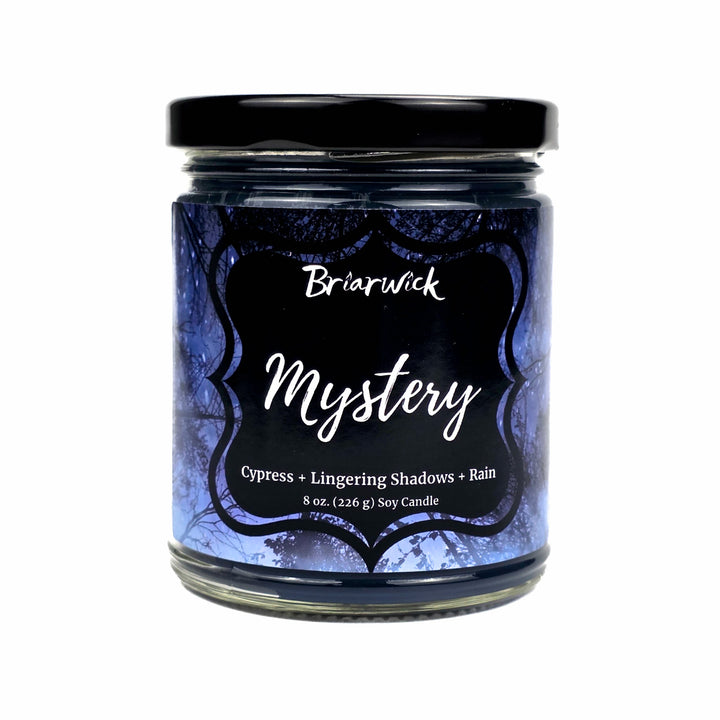 An 8 oz soy candle in a clear glass jar with a black lid set on a white background and a dark blue and black label reading 'Briarwick Mystery' and 'Cypress + Lingering Shadows + Rain'.