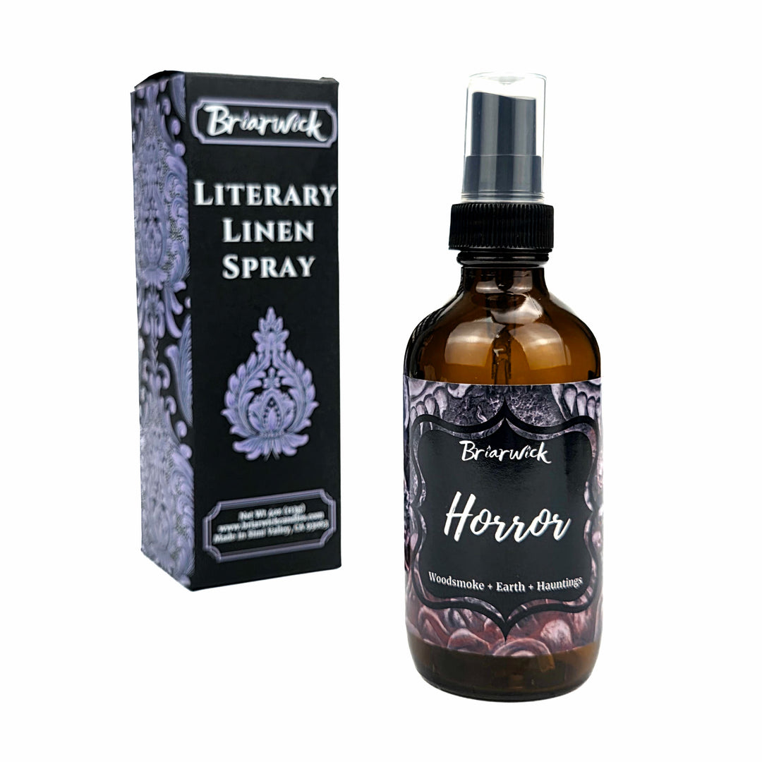 An amber glass spray bottle labeled 'Briarwick Horror Literary Linen Spray' stands next to its black and lavender patterned retail box on a plain white background.