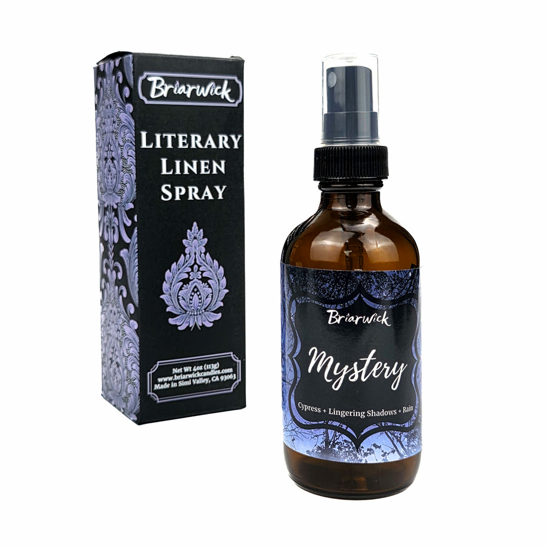 An amber glass spray bottle labeled 'Briarwick Mystery Literary Linen Spray' stands next to its black and lavender patterned retail box on a plain white background.