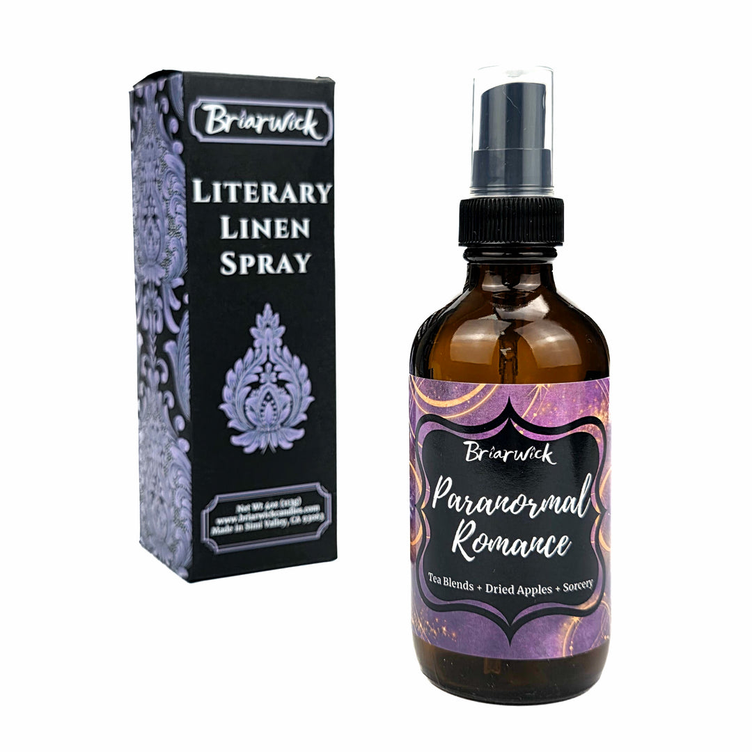 An amber glass spray bottle labeled 'Briarwick Paranormal Romance Literary Linen Spray' stands next to its black and lavender patterned retail box on a plain white background.