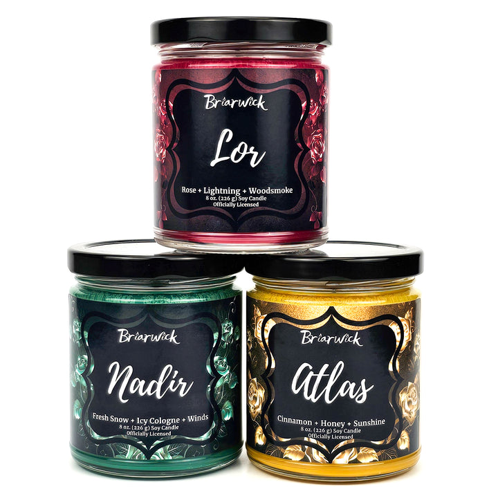 Three jar-sized candles with labels indicating different scents such as Atlas, Nadir, and Lor. The jars are decorated with gold, green, and red designs and the brand name Briarwick is visible on each.