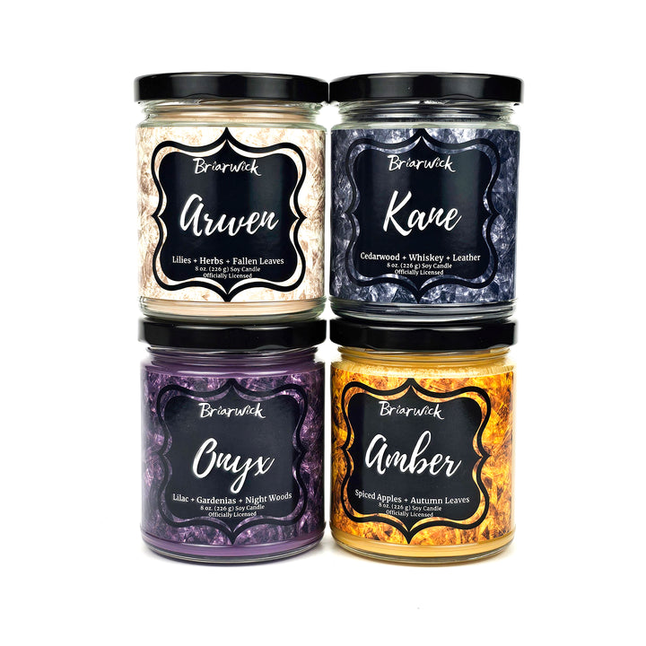 Group of colorful Briarwick candles from the Sacred Stones collection. Top row is the taupe colored Arwen candle and black Kane candle. Bottom row is the purple Onyx candle and yellow Amber candle. 