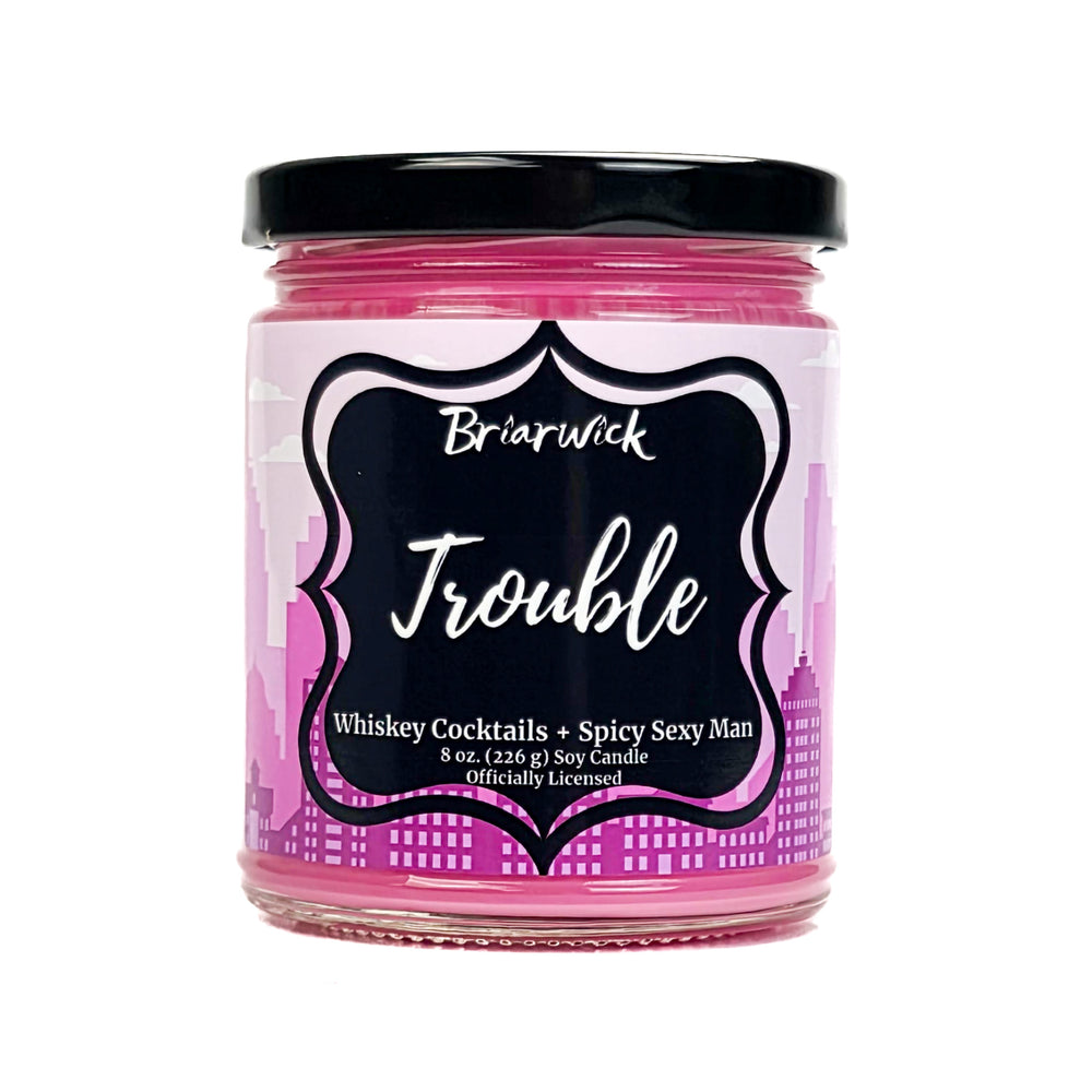 Pink candle jar with black lid and label called Trouble on a white background