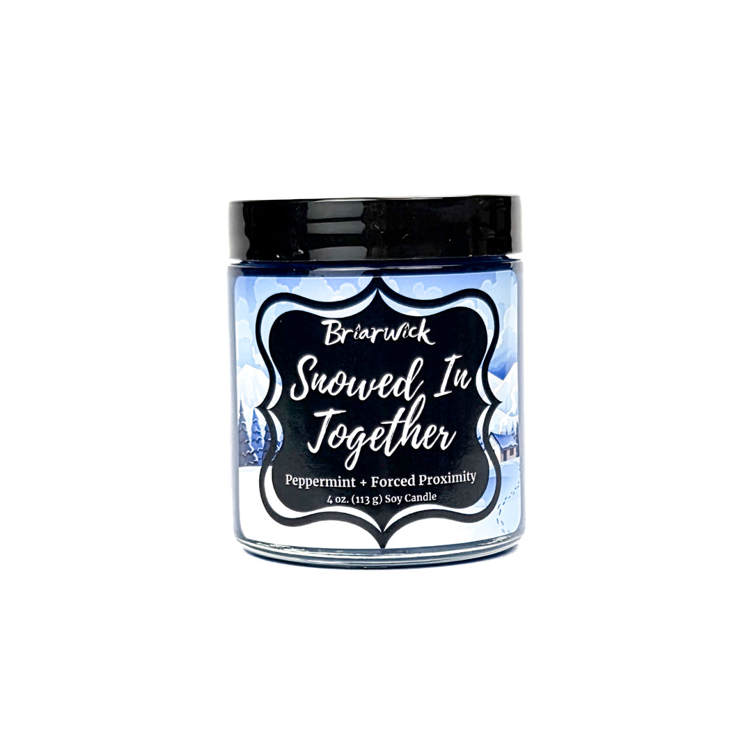 Snowed In Together 4oz colored candle with blue and white snow covered lodge design on a white background