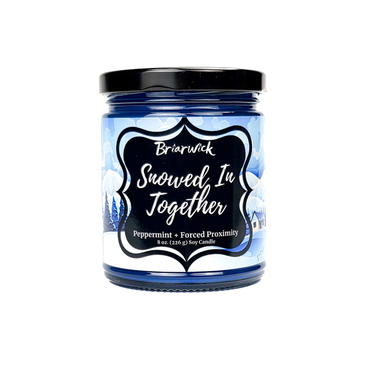 Snowed In Together 8oz colored candle with blue and white snow covered lodge design on a white background