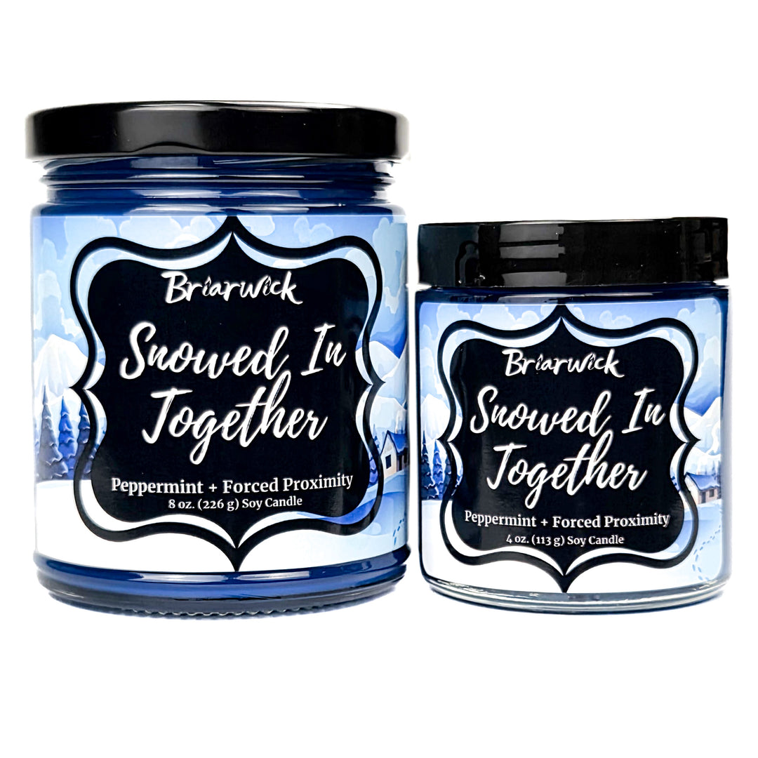 Snowed In Together 8oz and 4oz colored candle with blue and white snow covered lodge design on a white background